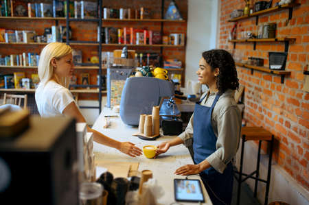 Female barista gives coffee to woman in cafe