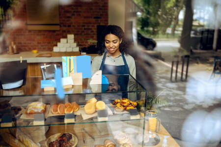 Female barista at showcase with desserts in cafe