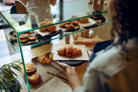 Barista takes croissant from showcase in cafeの写真素材
