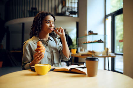 Student drinks coffee with croissants in cafeの写真素材