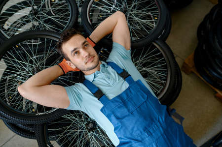 Worker lying on stack of bicycle wheels on factory