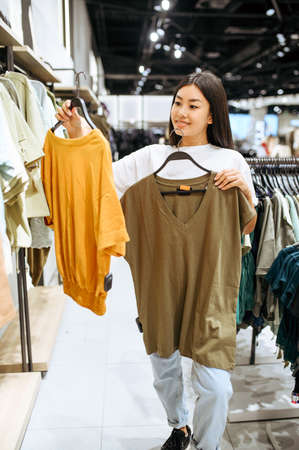 Cheerful woman choosing clothes in clothing store