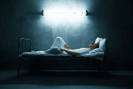 Psycho man lying in bed, dark room on backgroundの写真素材