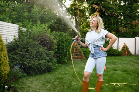 Smiling woman with hose watering trees in garden