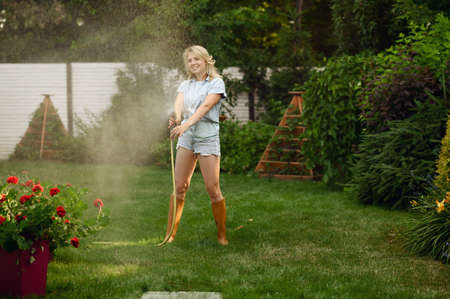 Gardener with hose watering plants in the garden