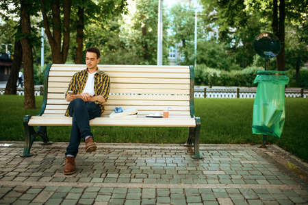 Young man sitting on bench among the trash in parkの写真素材