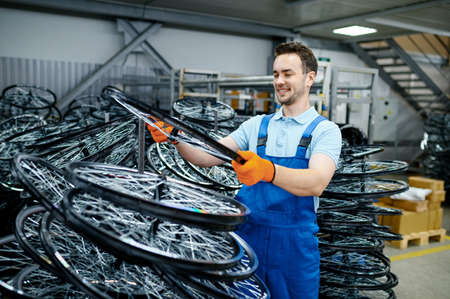 Mechanic in uniform holds bicycle wheel on factoryの写真素材