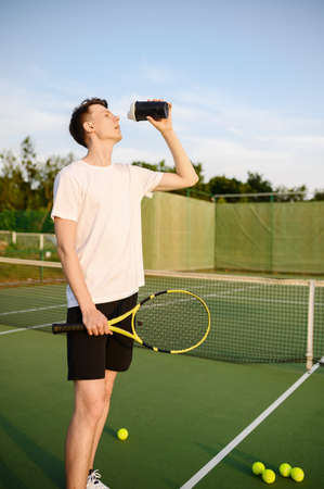 Tired male tennis player drinks waterの写真素材