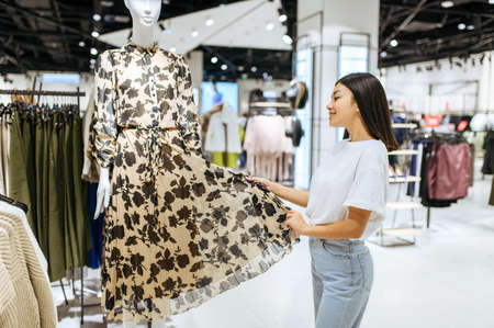 Cheerful woman choosing dress in clothing storeの写真素材