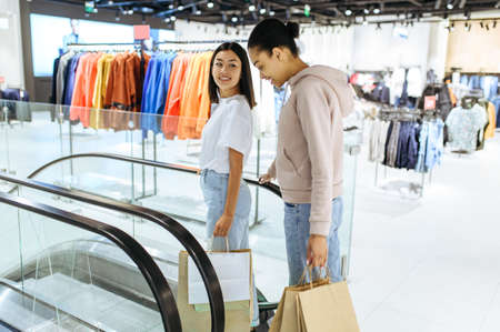 Happy girls with purchases in bags on escalator