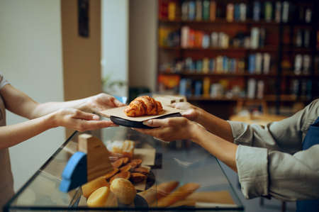 Female barista gives croissant to woman in cafeの写真素材