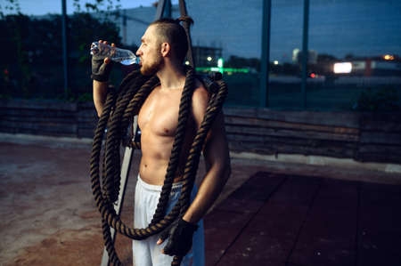 Muscular man with crossfit ropes drinks water