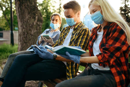 Young people in masks sitting on bench, quarantine