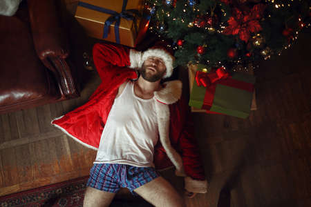 Bad Santa in underpants lying under christmas treeの写真素材