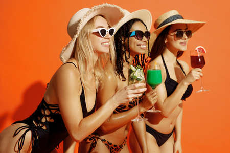 Three sexy women in swimsuits holds coctails