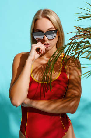 Sportive woman in red swimsuit poses on cyan