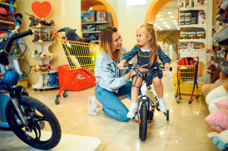 Mom and little girl buying bicycle in kids store