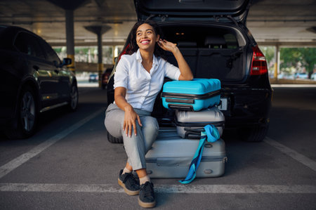 Happy woman sitting on suitcases in car parkingの写真素材
