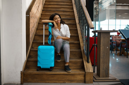 Woman with suitcase sitting on stairs in airportの写真素材