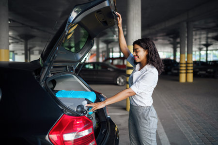 Young woman puts suitcases into the car on parking