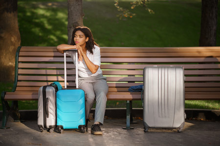 Woman with suitcase sitting on the bench in parkの写真素材