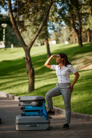 Cheerful woman with suitcase walking in parkの写真素材