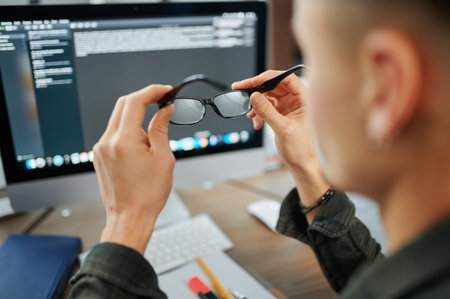 Male IT specialist holds glasses at pc monitorの写真素材