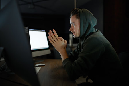 Young internet hacker in hood sitting at monitorsの写真素材
