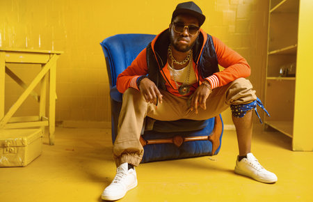 Rapper posing in chair in studio with yellow tonesの写真素材