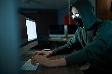 Male hacker in hood holds laptop, front view