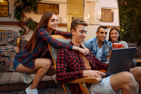 Friends using laptop near rv on picnic at camping