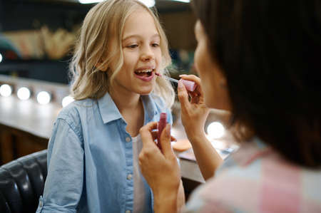Mother paints her daughter lips in makeup salonの写真素材
