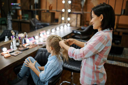 Mother doing hairstyle to her daughter in salonの写真素材