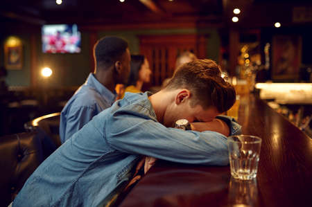 Friends drinks beer, man sleeps at counter in barの写真素材