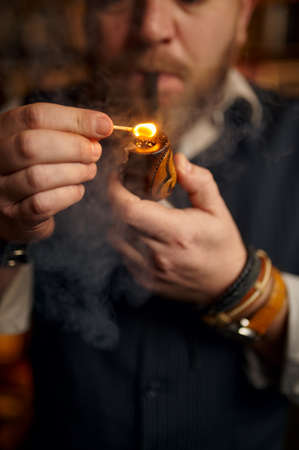 Bearded man lights smoking pipe with a match