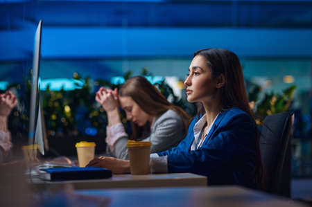 Tired women sitting at the table in night officeの写真素材