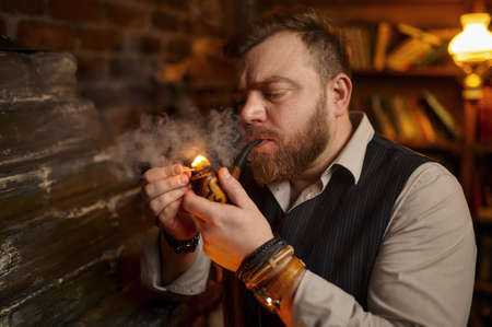 Bearded man lights smoking pipe with a matchの写真素材