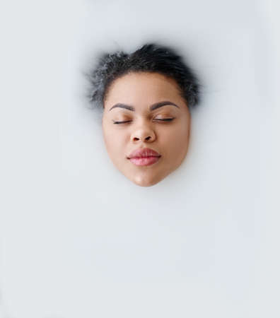 Woman lying in bath with milk, top view on faceの写真素材