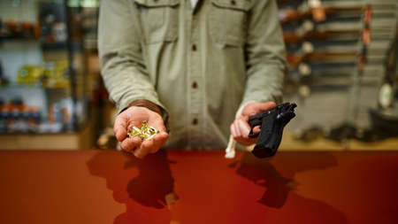 Man holds handgun and bullets in gun storeの写真素材