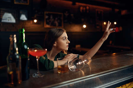 Depressed woman drinks alcohol at counter in bar
