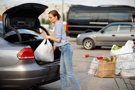 Woman with cart puts her purchases in car trunkの写真素材
