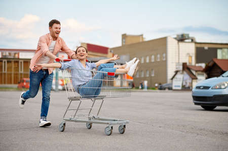 Funny family couple rides in cart on parkingの写真素材