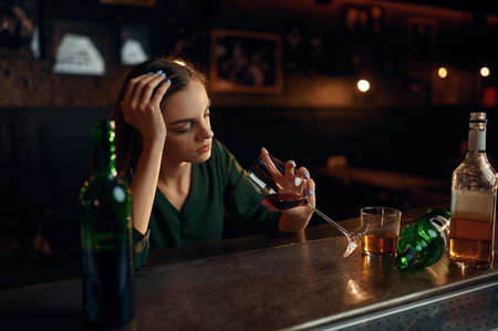 Unhappy woman drinks alcohol at the counter in barの写真素材