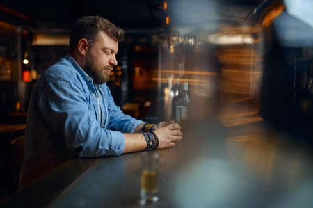 Stressed man drinks alcohol at the counter in barの写真素材