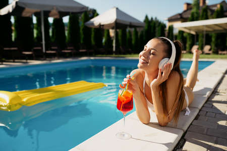 Woman in headphones drinks coctail at the pool