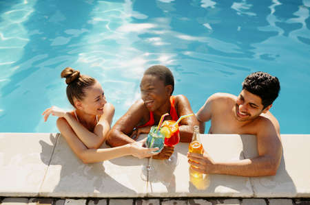 Friends with beverages pose at the edge of poolの写真素材