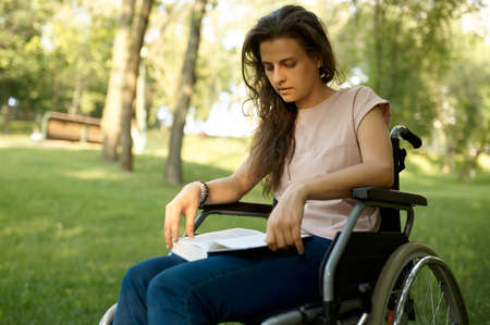Disabled woman in wheelchair reading book in parkの写真素材