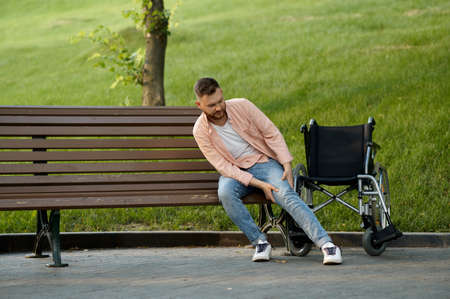 Disabled man transfers from wheelchair to a benchの写真素材
