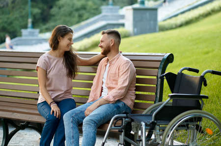 Couple with wheelchair relaxing on bench in parkの写真素材