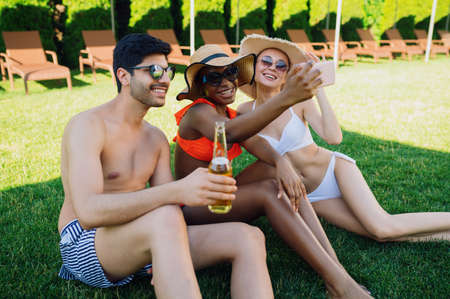 Cheerful friends drink beer near the pool